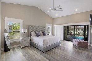 Une chambre avec un grand lit, une table de chevet, une lampe, un ventilateur de plafond et une vue sur une piscine, visible à travers une porte vitrée.