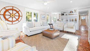 Ein geräumiges Wohnzimmer mit einer großen Wanddekoration aus Holzrädern, einem weißen Sofa, gestreiften Sesseln, einem Couchtisch und einem Bücherregal.
