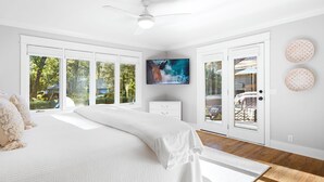 Ein Schlafzimmer mit einem großen Bett, einem Deckenventilator, einem Fernseher und Blick ins Freie durch große Fenster.