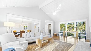 Ein geräumiges Wohnzimmer mit einem weißen Sofa, einem Holztisch und einem gemusterten Teppich. Es gibt einen Essbereich mit Tisch und Stühlen sowie einen Blick auf Grünflächen im Freien.