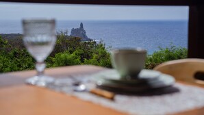 A table with a glass and cup, a plate, and a cinnamon stick, overlooking a rocky coastline and the sea. - Pousada Vila Nakau (Fernando de Noronha)