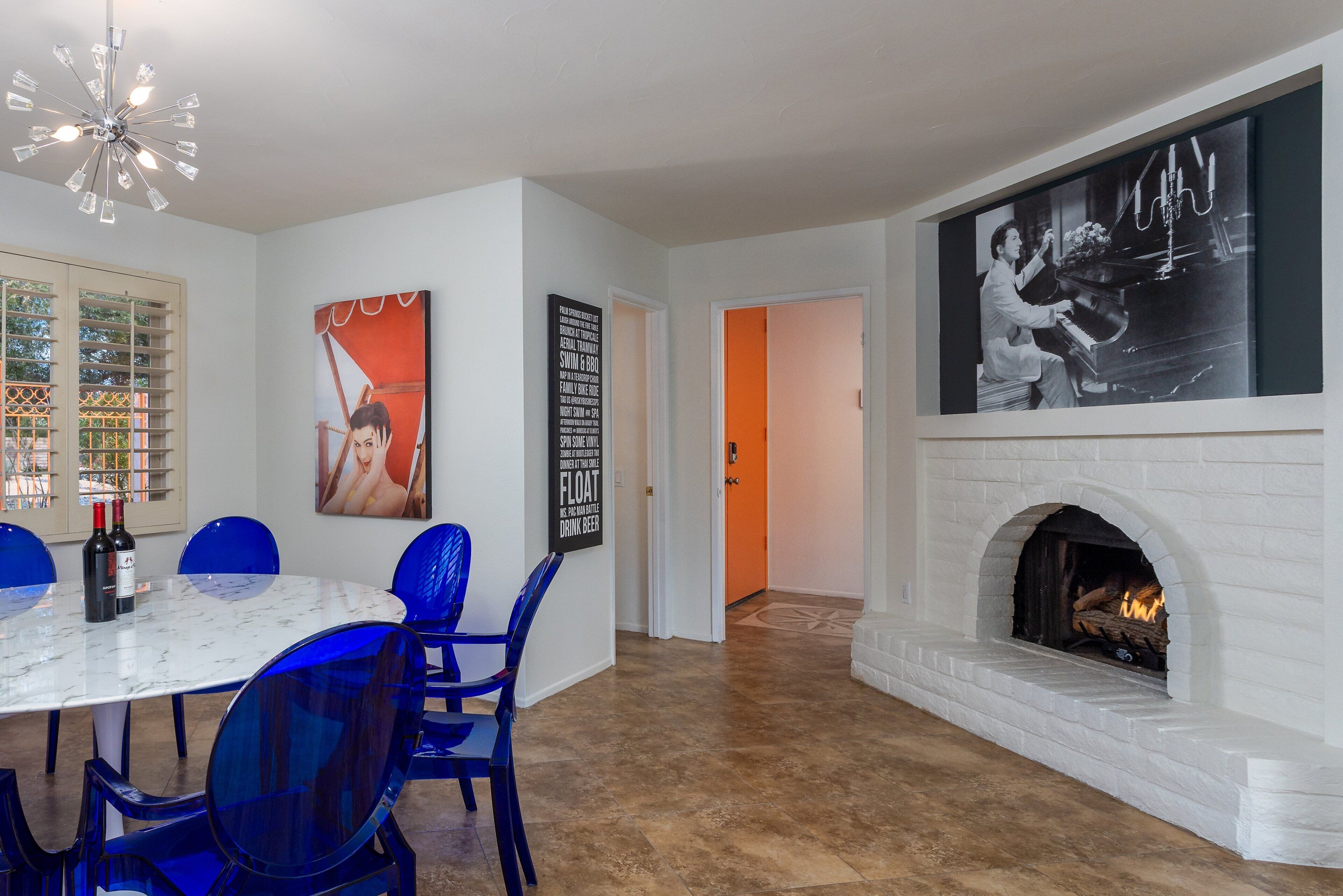 Un comedor con una mesa de mármol, sillas azules, una chimenea y una pared con una fotografía blanco y negro.