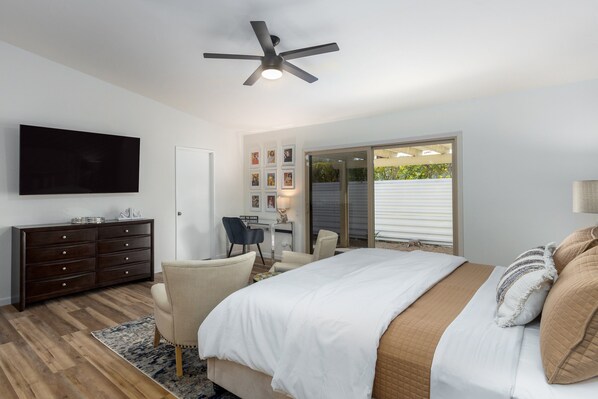 Ein Schlafzimmer mit Bett, Schreibtisch, Stuhl, Fernseher und Deckenventilator.