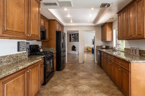 A kitchen with wooden cabinets, granite countertops, a stove, refrigerator, and a microwave. - Risky Business – Retro Cool Palm Springs (Palm Springs)