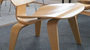 Una silla de oficina moderna con estructura de madera y asiento acolchado, sobre un piso alfombrado.