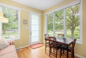 A dining area with a table and chairs, a door with a frosted glass panel, and a window with blinds. - 🏖️Sleepy Hollow Beach Resort, Cottage 3A – Family Fun on Lake Michigan! (South Haven)