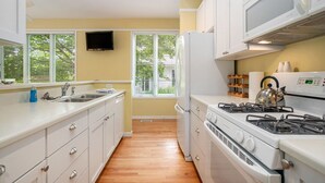 A kitchen with white cabinets, a stove, a refrigerator, and a window with blinds. - Sleepy Hollow Beach Resort, Cottage 3A – Family Fun on Lake Michigan! (South Haven)