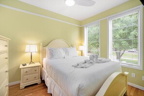 A neatly made bed in a room with a nightstand, a lamp, and a window with blinds. - 🏖️Sleepy Hollow Beach Resort, Cottage 3A – Family Fun on Lake Michigan! (South Haven)