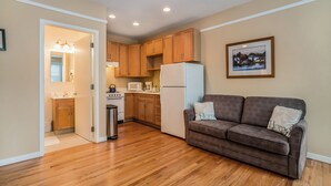A compact living space with a kitchenette, wooden cabinets, a white refrigerator, a brown sofa with 'Home' pillows, and a framed picture on the wall. - Sleepy Hollow Beach Resort, Cottage 3C – Family Fun on Lake Michigan! (South Haven)