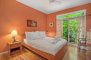 Un dormitorio con una cama de madera, una mesita de noche con lámpara, una ventana con cortinas y un balcón con silla.