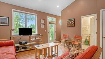 A living room with a television, wooden furniture, and large windows.