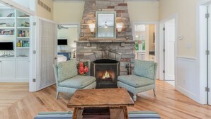 A living room with a stone fireplace, two patterned armchairs, a wooden coffee table, and a bookshelf.