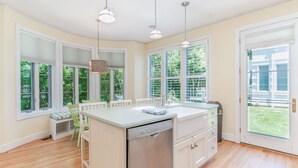 A kitchen with a dishwasher, white cabinets, and a window overlooking a green yard.