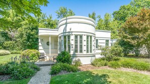 A modern house with a curved facade, surrounded by a well-maintained garden and trees.