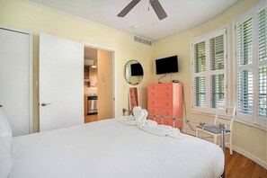 Un dormitorio con una cama, un tocador rosa, un televisor y una ventana con contraventanas.