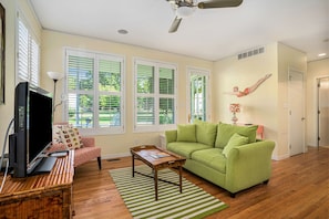 A living room with a green sofa, a wooden coffee table, a television, and a ceiling fan.