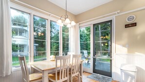 Un comedor con mesa y sillas de madera, ventanas amplias y una puerta que da al exterior.