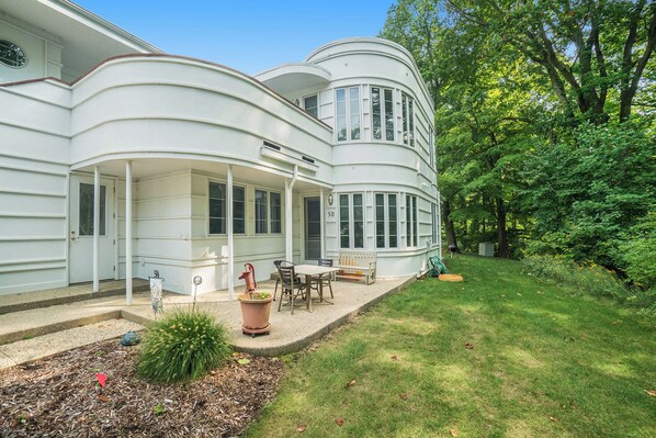 A white, curved two-story house with a covered patio, a small garden, and a lawn. - 🏖️Sleepy Hollow Beach Resort, Gateway 50 – Family Fun on Lake Michigan! (South Haven)