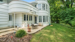 Una casa blanca de dos plantas con forma curva, un porche cubierto, un pequeño jardín y un césped.