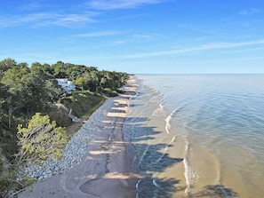 Una propiedad costera con un paseo pavimentado a lo largo de la playa, un muro de piedra y una casa con vista al mar.