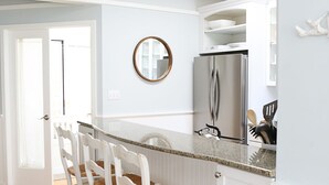 A kitchen with a white island, wooden chairs, and a refrigerator. - Sleepy Hollow Beach Resort, Cottage 8B – Family Fun on Lake Michigan! (South Haven)