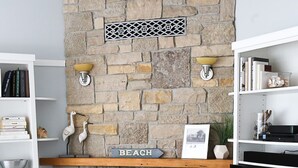 A living room with a stone fireplace, two teal armchairs, a bookshelf, and a flat-screen TV. - Sleepy Hollow Beach Resort, Cottage 8B – Family Fun on Lake Michigan! (South Haven)