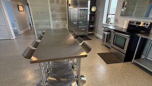 Une cuisine moderne dotée d’appareils électroménagers en acier inoxydable, d’une grande table et de luminaires suspendus.
