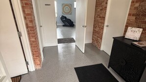 Un couloir avec un tapis noir, un fauteuil de massage et un mur sur lequel est affiché un panneau indiquant la présence d’un réseau « Wi-Fi ».