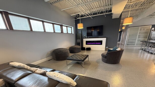 Un salon moderne comprenant un canapé en cuir, un pouf et des fauteuils ronds, un téléviseur à écran plat et une cheminée.