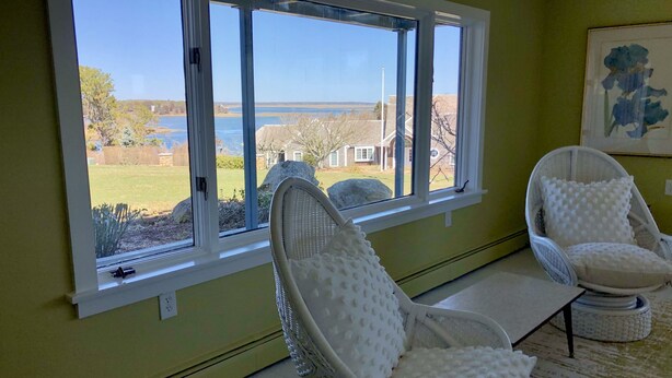 Ein Zimmer mit einem großen Fenster, zwei weißen Korbstühlen und einem Gemälde an der Wand.