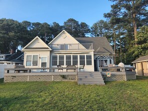 A two-story house with a covered porch, a deck, and a small outdoor seating area. - Waterfront home with dock, gazebo, and fenced yard (Lewes)