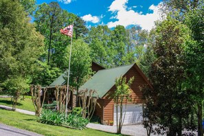 A cabin with a green roof, surrounded by lush greenery and a flag. - A Cowpoke's Dream 3 Bedroom Cabin by RedAwning (Sevierville)