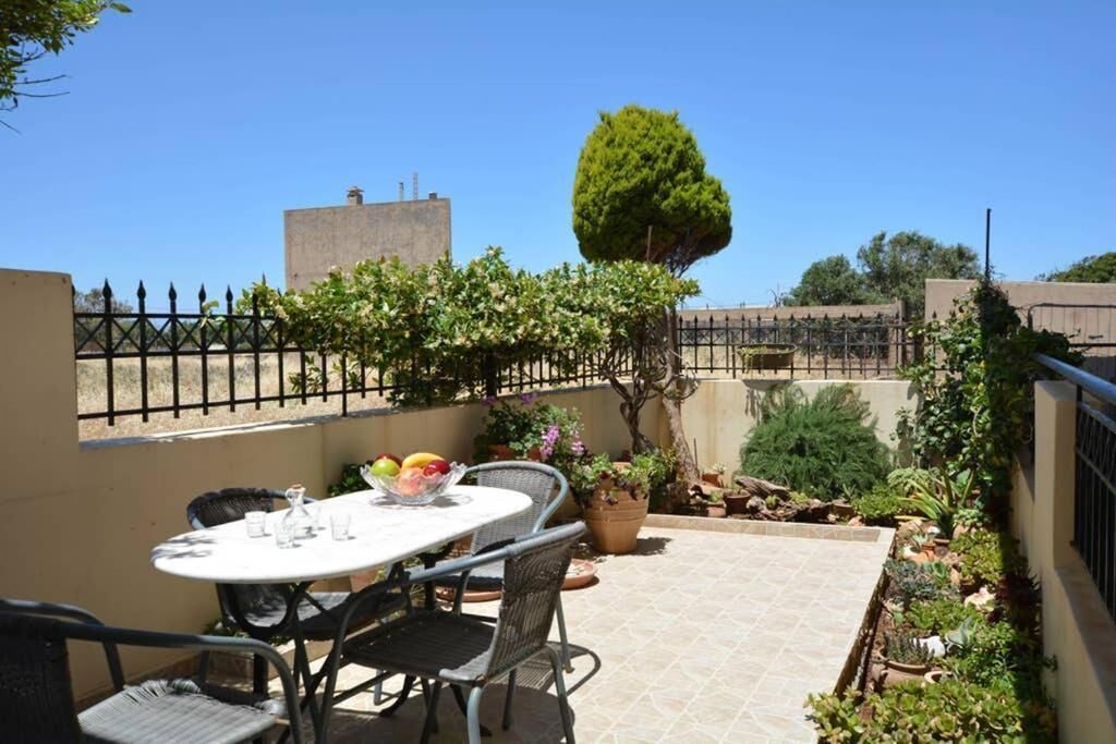 Un patio con una mesa redonda y sillas, rodeado de macetas con plantas y un pequeño árbol.