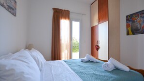 A hotel room with a bed, a window with curtains, a door, and a painting on the wall. - Olive Oil Residence (Hersonissos)