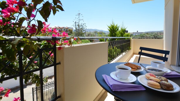A balcony with a table set for breakfast, including coffee, pastries, and a bowl of fruit. - Olive Oil Residence (Hersonissos)