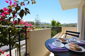 A balcony with a table set for breakfast, including coffee, pastries, and a bowl of fruit. - Olive Oil Residence (Hersonissos)