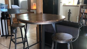 Ein Essbereich mit einem runden Holztisch, zwei Metallhocker und einer Couch.