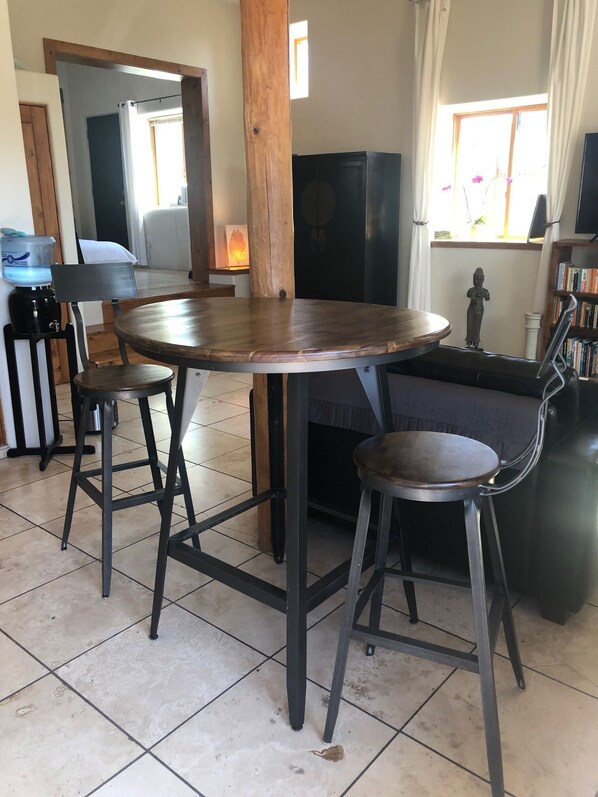 A dining area with a round wooden table, two metal barstools, and a sofa.
