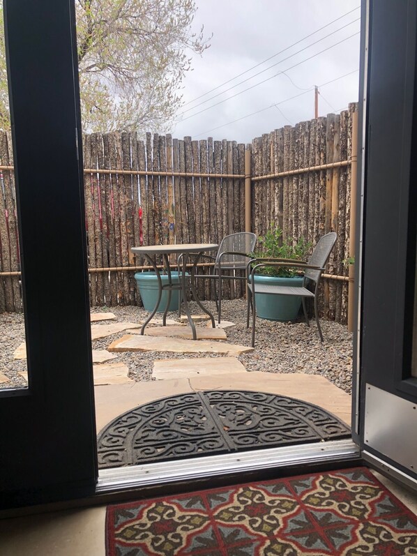 A patio area with a table and chairs, a wooden fence, and a door with a patterned mat.