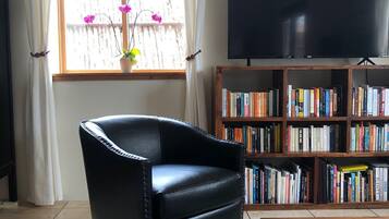 A living room with a leather armchair, a bookshelf filled with books, a television, and a coffee table with a remote control.