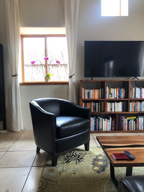A living room with a leather armchair, a bookshelf filled with books, a television, and a coffee table with a remote control.