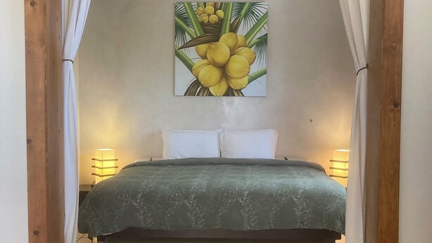 Ein Schlafzimmer mit einem Bett, einem Deckenventilator und einem Bild von gelben Blumen an der Wand.