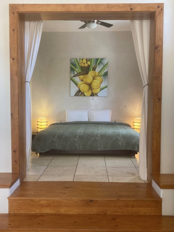 Une chambre à coucher avec un lit, un ventilateur de plafond et un tableau représentant des fleurs jaunes accroché au mur.
