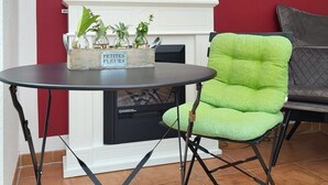 Una sala de estar acogedora con chimenea, un sillón verde y una pequeña mesa con un cartel que dice "PETITES FLEURS".