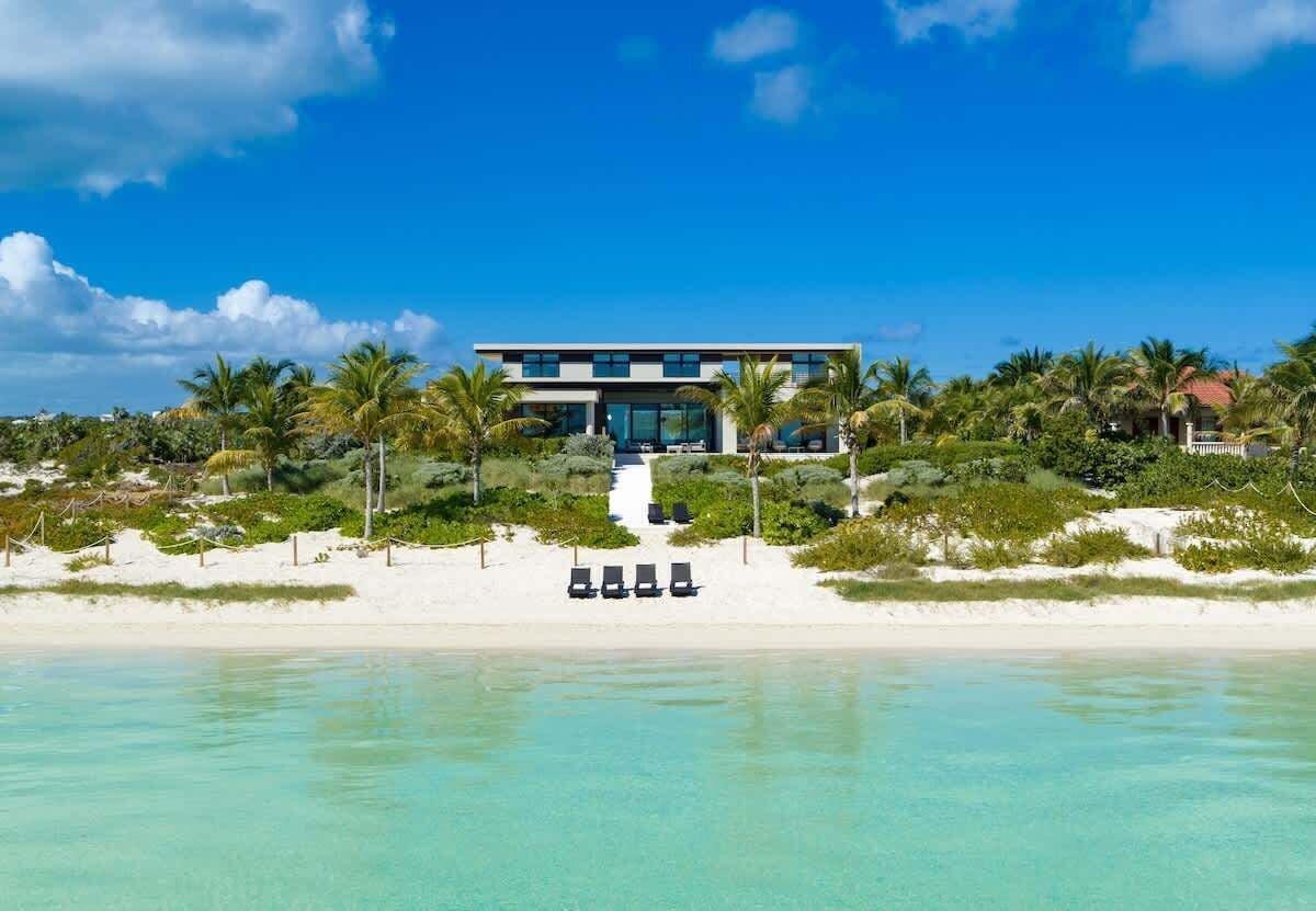 Une propriété moderne située en bord de mer, comprenant un bâtiment à deux étages, une plage de sable et des palmiers.