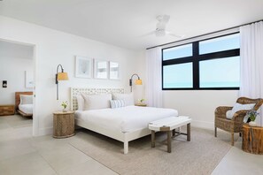 A modern bedroom with a large bed, bedside lamps, a ceiling fan, and a view of the sea through a large window. - Beachfront Villa w/ Pool, Hot Tub & Tennis Court (Long Bay)