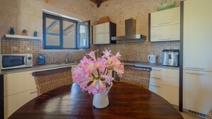 A kitchen with a wooden table, white cabinets, a microwave, and a vase with flowers. - Afrati villa (Zakynthos)