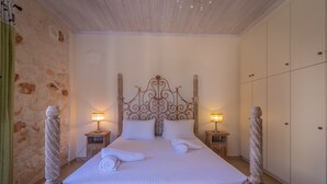 A neatly made bed with pillows and towels, wooden headboard, bedside lamps, and a stone wall. - Afrati villa (Zakynthos)