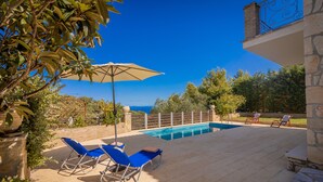 A pool area with lounge chairs and an umbrella, surrounded by stone walls and greenery. - Afrati villa (Zakynthos)