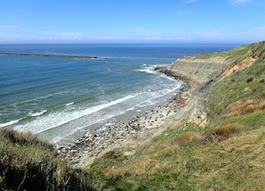 Un paysage côtier caractérisé par une rive rocheuse, une longue jetée s’avançant dans la mer et une colline verdoyante.